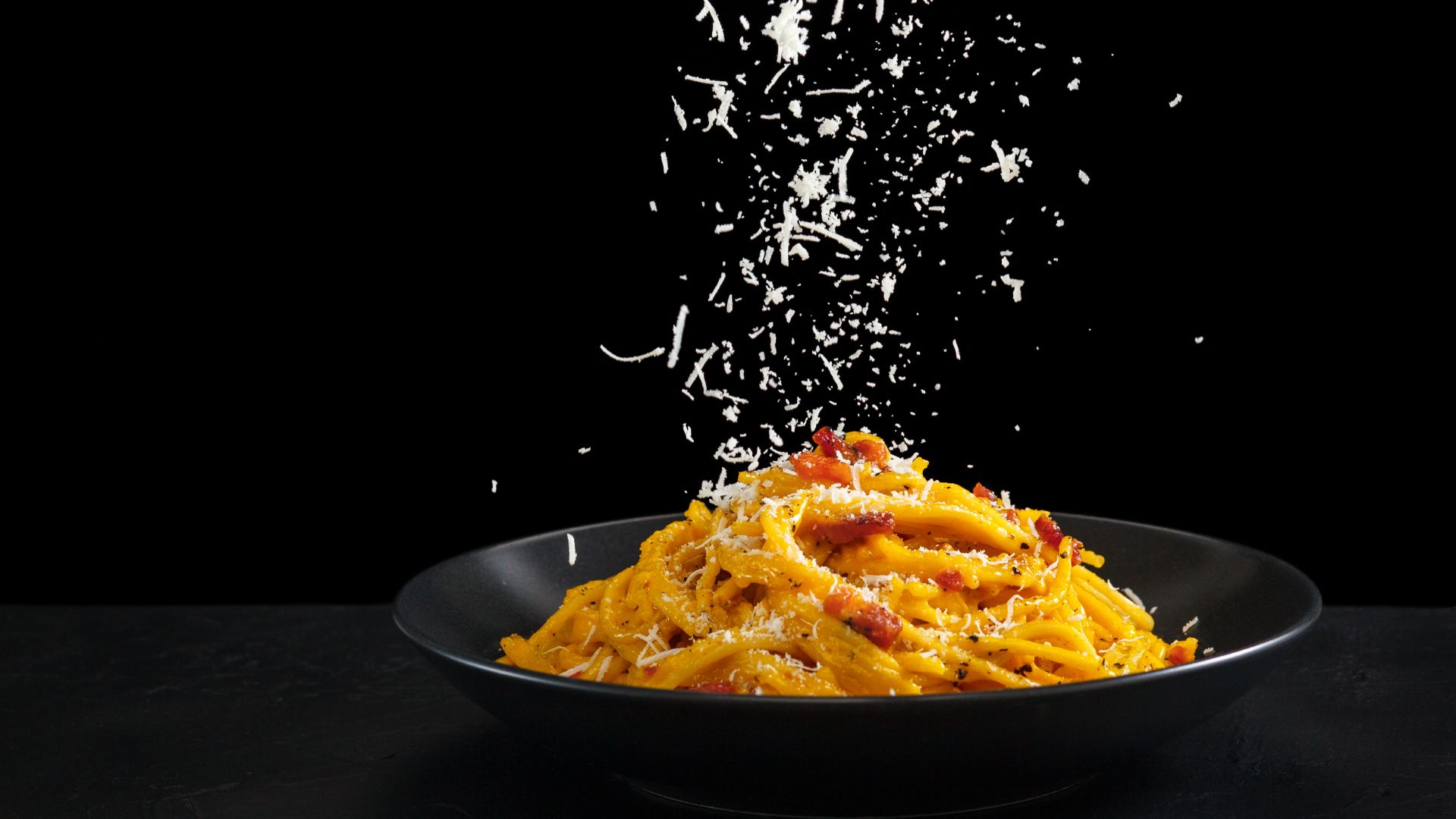 Pasta in a bowl being sprinkled with cheese